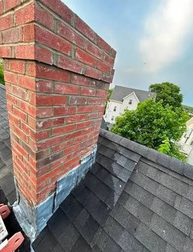 Repointed brick chimney rising above a shingled roof